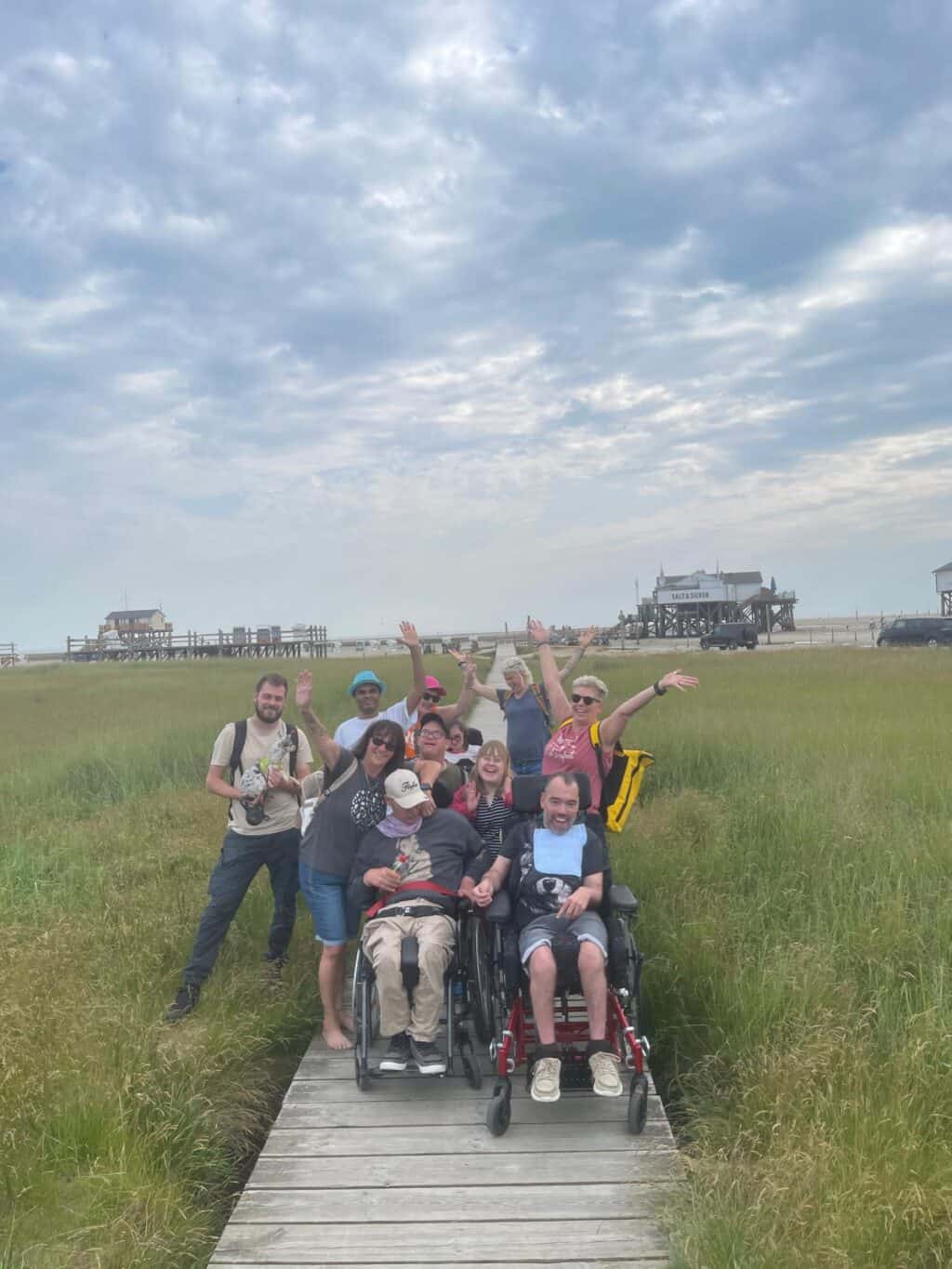 Eine Ausflugsgruppe jubelt auf einem Holzsteg in einer Wiesenlandschaft.