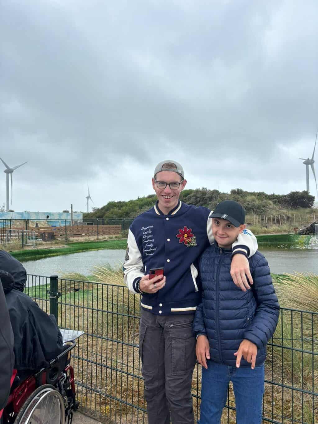 Zwei Personen stehen eng umarmt vor einer windigen Küstenlandschaft.