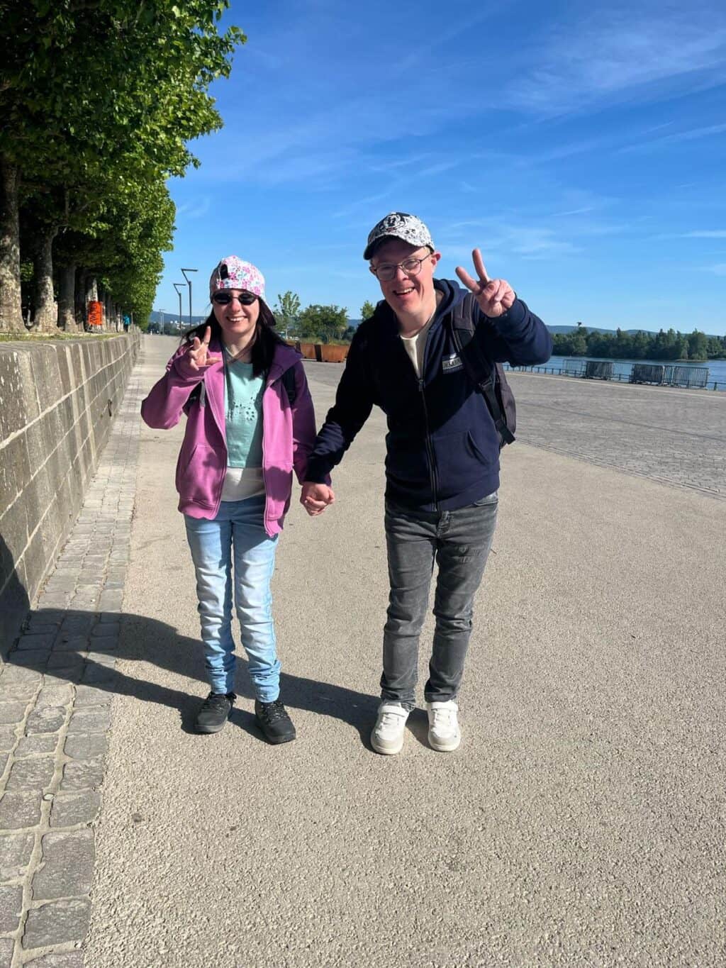 Zwei Personen spazieren Hand in Hand am Wasser entlang.