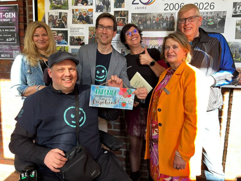 Eine Gruppe steht zusammen und hält ein Schild hoch. Alle gucken fröhlich.