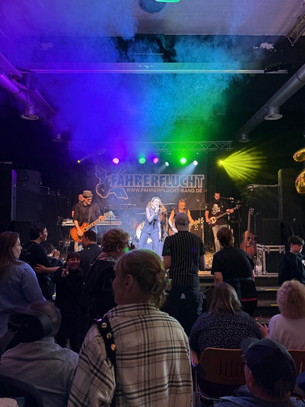 Viele Menschen stehen vor einer Bühne. Auf der Bühne spielt eine Band.