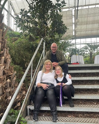 Drei Personen sitzen gemeinsam auf einer Treppe und schauen freundlich in die Kamera.